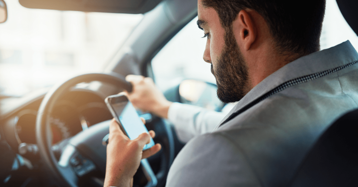 Distracted male driving with a smart phone on his hand