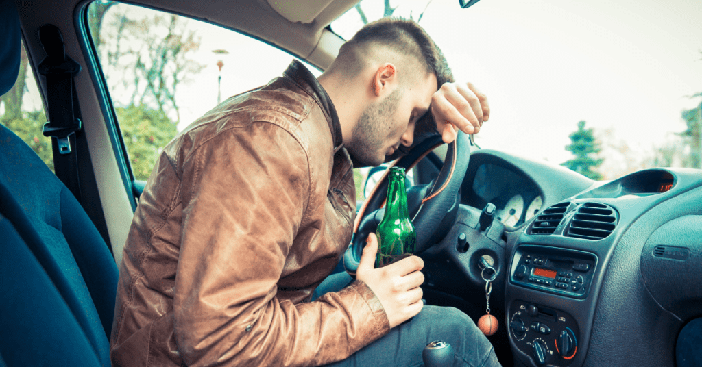 Drunk male driver with a bottle of beer on his hand and his head on the car wheel